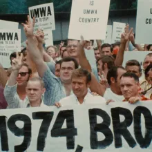 A crowd of white men holding signs promoting "UMWA" and raising arms