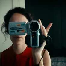 A reflection of a woman in a red, sleeveless top holding a Sony camcorder in front of her face