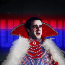 A man's face (Brian Mulroney) is inserted over a red cape with blue frills and white feathers, placed over a black background which displays the word MULRONEY, the bottom two-thirds of the text colored blue and the top two-thirds colored pink