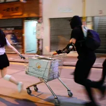 A still from 'Do Not Split', nominated for Best Documentary Short at the 93rd Academy Awards. The frame shows three young protestors in Hong Kong running down an empty street with a shopping cart.