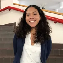 Arlet is a brown-skinned Latina, and she is posing in front of a staircase.