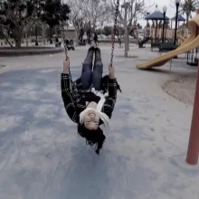 A woman from the film swings on  a swing in the middle of a playground; her head is upside-down as she faces the camera.