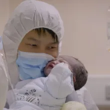 An Asian man, wearing a protective hood and mask, holds his newborn baby. From Yung Chang's 'Wuhan Wuhan."  Courtesy of Stars Collective Films Entertainment Group, Inc.
