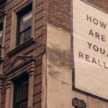 Stock image of a brownstone building with the words ‘How Are You, Really?’ painted on its side wall. Courtesy of Finn/Unsplash