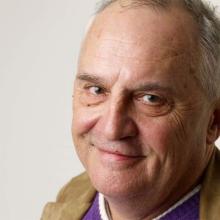 Headshot of John Zaritsky, a white male filmmaker, with gray hair. He is wearing a purple sweater and tan jacket. Photo courtesy of Matt Carr/Getty Images.