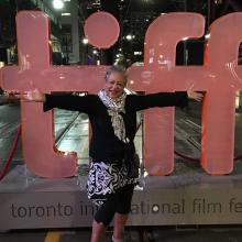 Michelle Materre is an African-American woman with short gray hair. She is standing in front of the signage of the Toronto International Film Festival. Photo courtesy of Julie Dash.