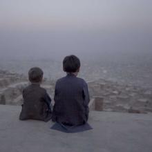 Young Afghani boys, Afshin and Benjamin, sit with their backs to the camera looking out at the city of Kabul. From Aboozar Amini’s ‘Kabul, City in the Wind.’ Courtesy of Movies that Matter.