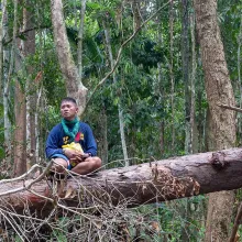 A middle-aged Filipino male activist sits on a fallen tree trunk; he is wearing shorts and a blue t-shirt that says "Palawan para-EnviFORCER." . Photo from Karl Malakunas' 'Delikado.' Courtesy of Hot Docs.