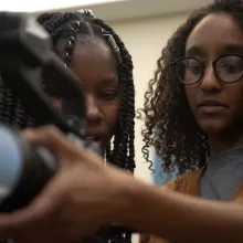 Two Black women students look into a video camera screen. Photo credits Marco Marco Poggio.