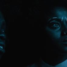 Two young Afro-German women photographed in low light. They have white traditional markings drawn on their faces. Image from Anna Zhukovets’ and Kokutekeleza Musebeni’s ‘Door of Return’. Courtesy of BlackStar Film Festival.