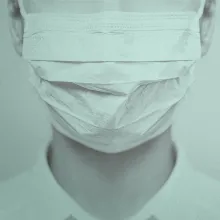 A close up shot of a woman with white skin wearing a white face mask.