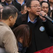 An activist, holding a microphone and wearing a black blazer over a blue shirt, addresses a protest in Brooklyn, New York.