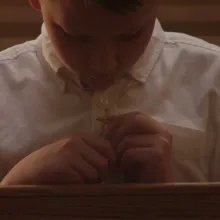 Terrick Trobough is a young white male actor wearing a white shirt, sitting on a church bench. He is wearing a cross. Image from Robert Greene’s ‘Procession.’ Courtesy of Netflix.