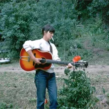 Karen Dalton is a white woman in a white sweater and blue jeans. She is playing a guitar and smoking a cigarette. Image from Richard Peete and Robert Yapkowitz’s ‘Karen Dalton: In My Own Time.’ Courtesy of The 2050 Group.