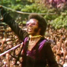 Sly Stone, a Black male musician in violet and black, plays to a huge crowd in Questlove’s ‘Summer of Soul’ (Director: Questlove; Producer: David Dinerstein, Robert Fyvolent, Joseph Patel) Courtesy of Cinetic Media.