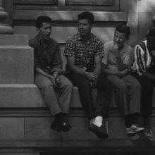 A BW photo of four young boys—one Black, three white—sitting on a building ledge