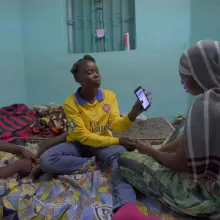 Three African girls sit in a room with a turquoise background as one shows her phone. From Ousmane Samassékou’s 'The Last Shelter.' Photo courtesy of STEPS. 