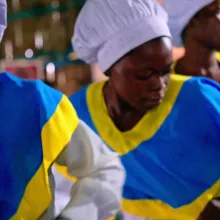 African women chefs in white hats and blue and yellow uniforms.