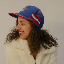 A photo of filmmaker Justine Armen, a mixed-race woman with dark brown curly hair wearing a blue and red baseball cap and white coat, looking to the side and smiling.