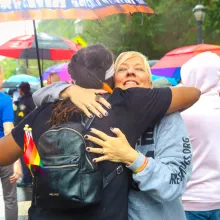  A mother from the mama bears movement hugs a person wearing a black backpack with rainbow pride flags hanging from it during a pride celebration. Photo courtesy of Mama Bears.