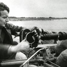 A black and white photo of Mark Soosaar facing a camera at the ocean. 