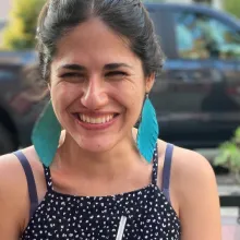 Mexican-American woman smiling with dark hair, wearing a black and white polka dot dress and teal earrings.