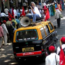 Anand Patwardhan, an Indian man with long white hair, seated atop a van that is moving through the street, is filming 'Jai Bhim Comrade' (2011). Courtesy of Anand Patwardhan. Photo: Priyanka Borpujari 