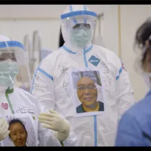 Two medical workers from Yung Chang’s ‘Wuhan Wuhan’ wear masks, bodysuits, and face shields with printed images of themselves on their chests in order to still be recognizable under all their safety wear. Courtesy of Stars Collective Films Entertainment Group Inc.