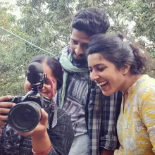 Three filmmakers from 'Writing with Fire' standing outdoors, smiling, looking at footage on a camera. 