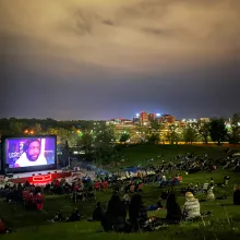 An outdoor nighttime screening: the audience sits on a grassy hill