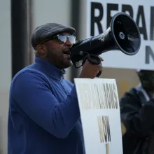 A Black man, wearing a blue polar fleece, leads a protest calling for reparations for victims of the 1921 Tulsa Massacre.