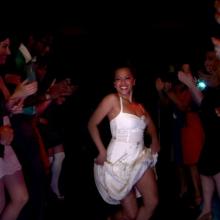 A woman in a white dress dances while people clap around her.  From Mathew Ramirez Warren’s 'We Like It Like That.' Courtesy of 'We Like It Like That' and 'America ReFramed.'