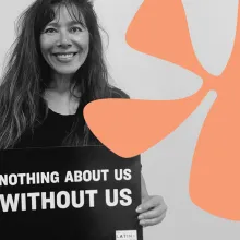 Maria Agui Carter holding a sign with "NOTHING ABOUT US WITHOUT US." 