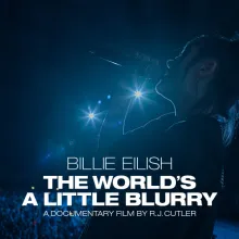 Billie Eilish singing to a crowd with blue lights shining in the background