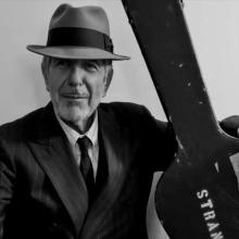 An image from Hallelujah: Leonard Cohen, A Journey, A Song, Leonard Cohen is wearing a fedora and holding a guitar in a black & white photo. 
