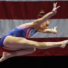 A gymnast in the middle of a routine, A large US flag is behind her