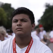 A dark skin-toned teenage boy in white tshirt, wearing red lanyard