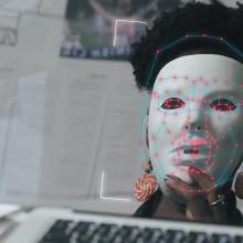 A person wearing a white mask in front of a computer camera