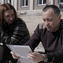 A woman and a man are sitting on the steps of a building, discussing a document