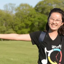 A young Chinese woman is smiling, holding her arms out on a grassy lawn