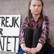 A young teenage girl sitting by a wall with protest sign next to her