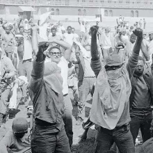 A black and white picture of a group of men with their firsts raised in the air.