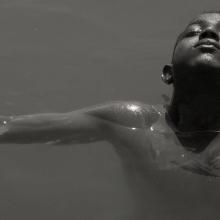 A black and white picture of a boy with Black skin swimming in water.