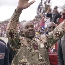 A man with Black skin and a patterned shirt addresses a large crowd.