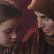 A woman in a brown hijab talks to a little girl.