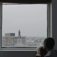 A man stares out the window at a large statue of a person.