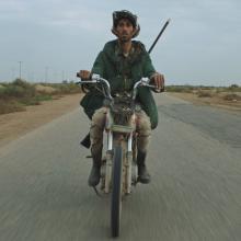 A brown-skin-tonned man in green parka riding a motorcycle