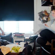 An artist is drawing, her subject sitting across from her on the couch