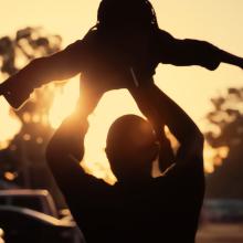 A man is lifting up a child against sunset