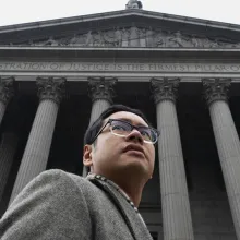 An Asian American man in grey suit in front of the courthouse
